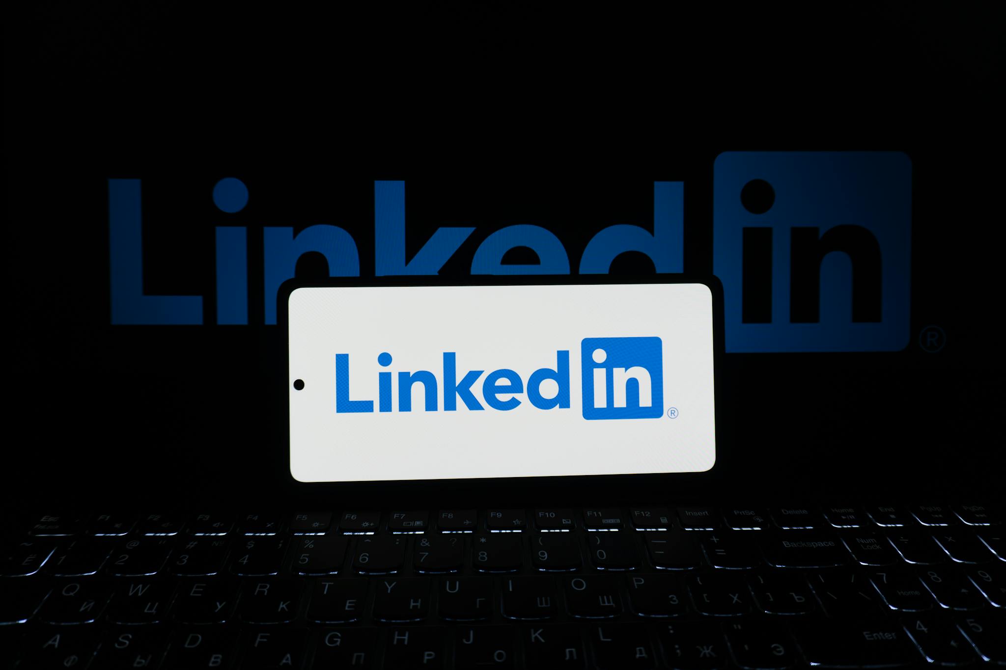 Smartphone showing LinkedIn logo with keyboard and large background logo, business theme.